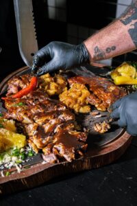 Les mains d'un chef assaisonnant un plateau de viande grillée avec des accompagnements, transmettant ainsi son expertise culinaire.