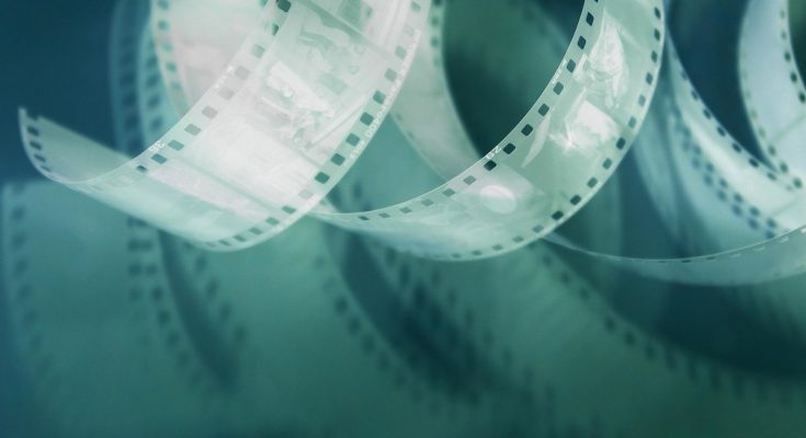 Film enroulé avec bandes de pellicule et éclats de lumière sur fond sombre
